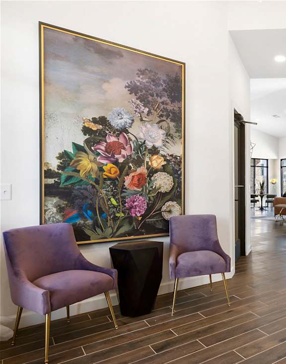 A room with a purple chair and a painting of flowers on the wall.