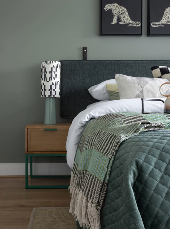 A bedroom with a bed, nightstand, and two framed pictures on the wall.