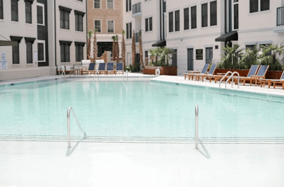 A swimming pool with lounge chairs and palm trees in the background.