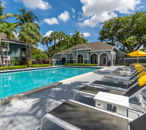 a swimming pool with yellow chaise lounge chairs in front of an apartment building