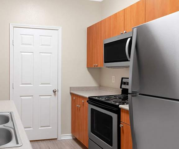 A cozy, modern kitchen with stainless steel appliances, light countertops with lots of room, and large wooden cabinets at the Landing at Mansfield Apartment Homes. 