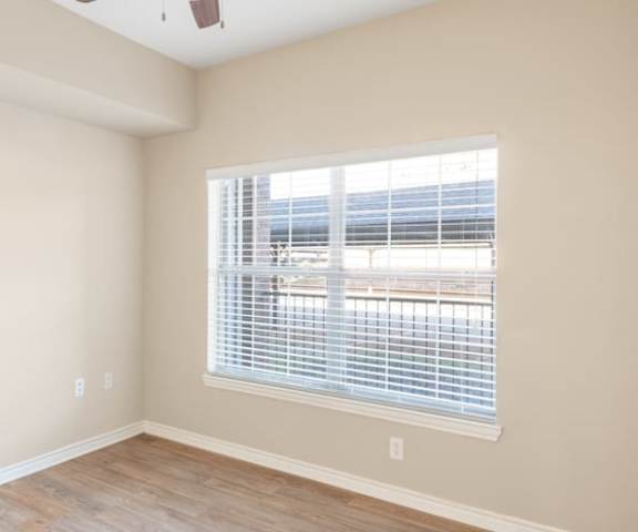 A large, empty hardwood floor bedroom with overhead lighting and a window at the Landing at Mansfield Apartment Homes. 