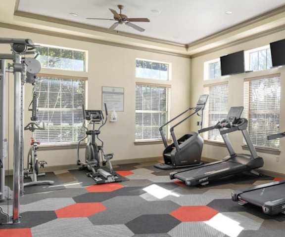 A spacious gym with cardio machines, windows, TVs, and weights at the Landing at Mansfield Apartment Homes. 