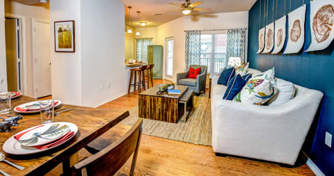 a living room and dining room with a wooden table and chairs and a blue accent wall at Villa Espada Apartments, San Antonio, Texas