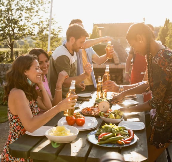 A group of people are gathered around a picnic table enjoying food and drinks.