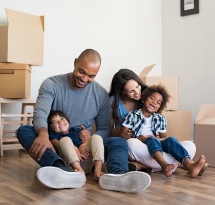 A family of four sitting on the floor surrounded by moving boxes.