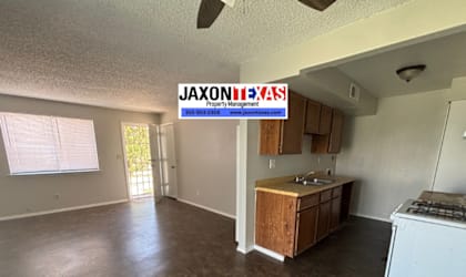 A JAXON REALTY sign is on the wall of a large, empty room with a kitchenette.