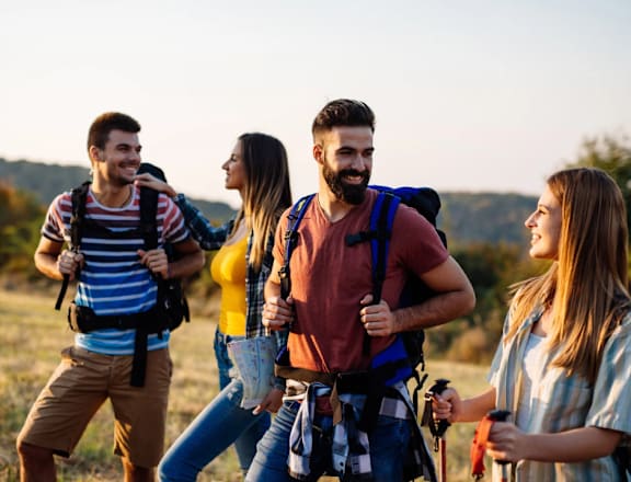 Four hikers with backpacks are walking through a field.