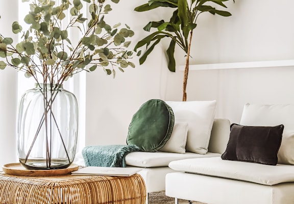 A living room with a white couch, a wicker table, and a vase with greenery.