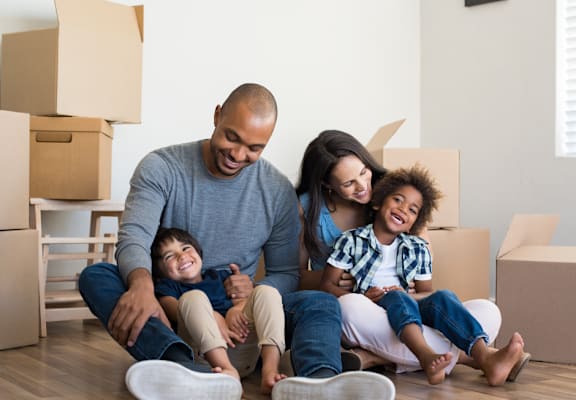 A family of four sitting on the floor surrounded by moving boxes.