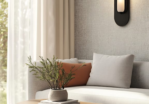 A modern living room with a grey sofa, a grey cushion, a grey pillow, a grey wall, a grey curtain, a grey table, a grey vase, a grey plant, a grey book, a grey wall