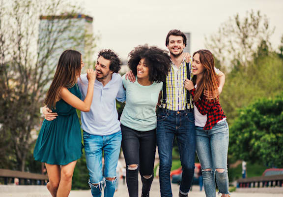 A group of five friends are walking together in a park.