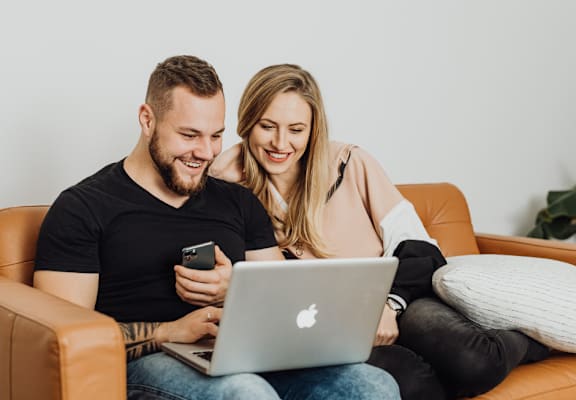 a man and woman sitting on a couch with a laptop computer