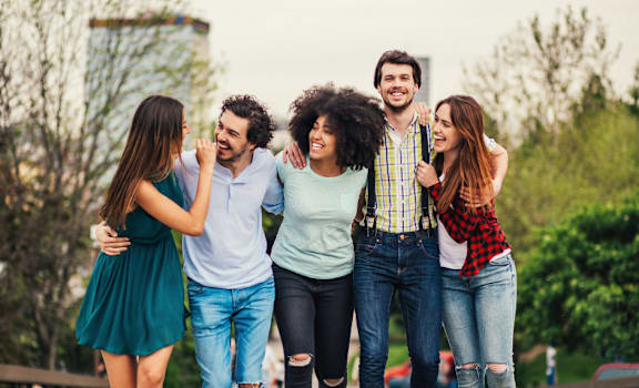 A group of five friends are walking together in a park.