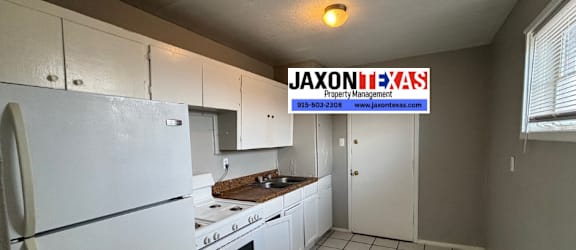 A kitchen with white appliances and cabinets with a JAXON B.A.S.S Property Management sign in the background.