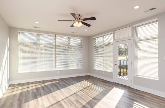 an empty living room with a ceiling fan and windows