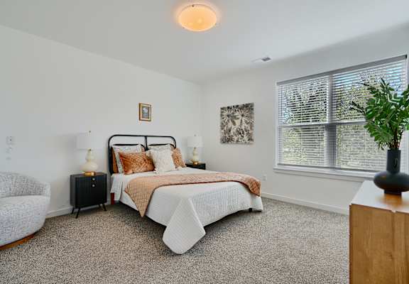 A bedroom with a bed, chair, and window.