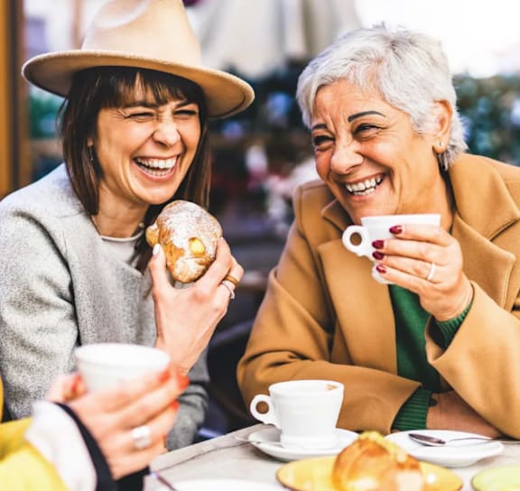 Three people are sitting at a table, laughing and enjoying pastries and coffee.