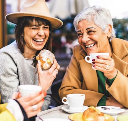 Three people are sitting at a table, laughing and enjoying pastries and coffee.