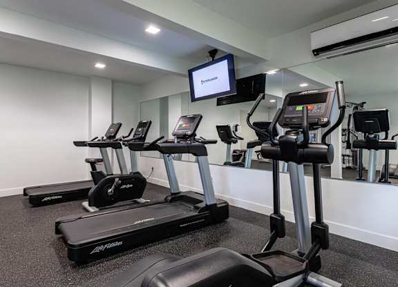 A gym with treadmills and a television mounted on the wall.