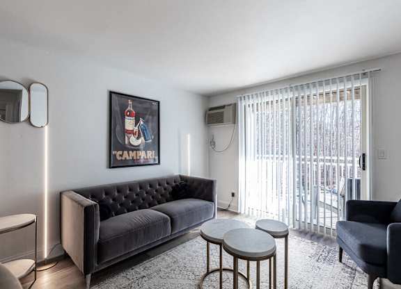 A living room with a black sofa, a grey armchair, a small table, and a framed picture on the wall.