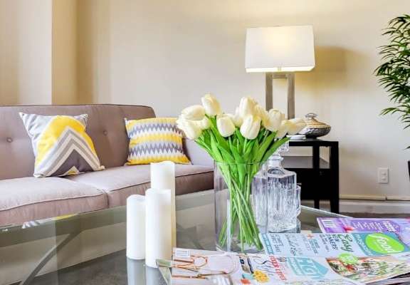 A living room with a grey couch, a glass table, and a vase of white flowers. at Ashton Heights Apartments, Suitland, MD