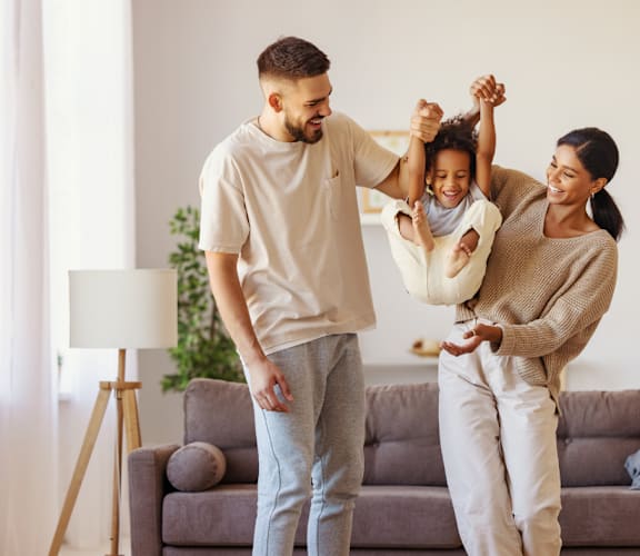 a young couple dances with their daughter while standing in their living room