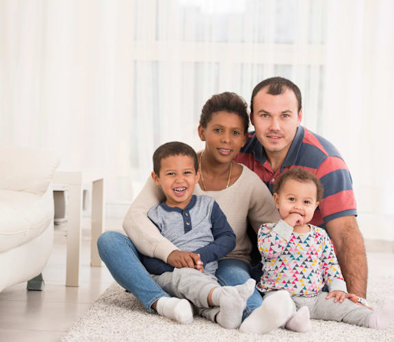 a family of four sitting on a rug in a living room