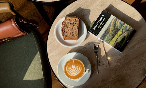 A table with a cup of coffee, a book, and a piece of cake on it.