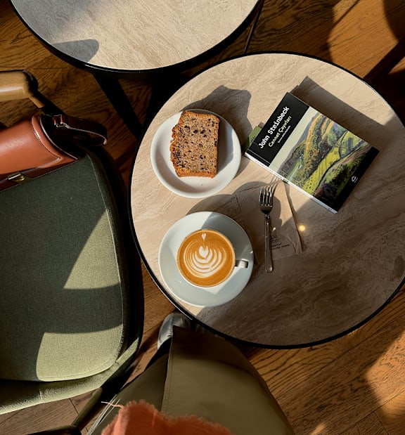 A table with a cup of coffee, a book, and a piece of cake on it.