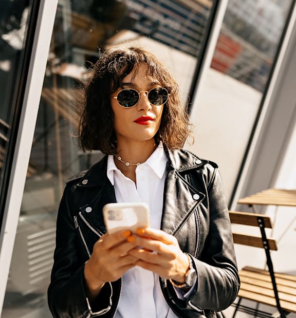 A woman in a black leather jacket is looking at her phone.