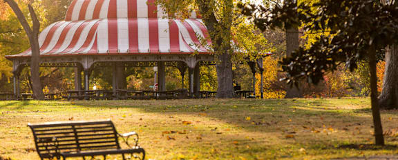 A wooden bench sits in front of a striped pavilion in a park.