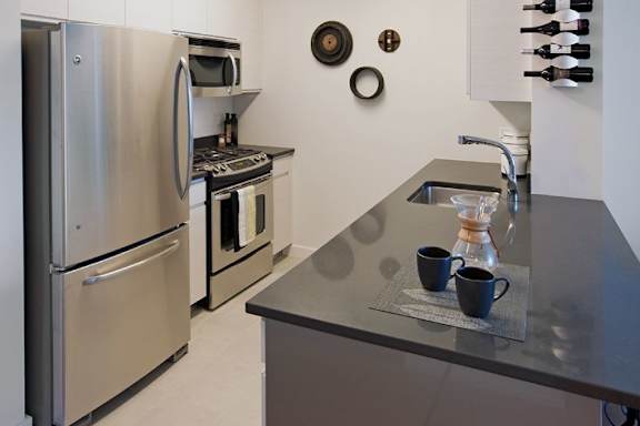 A modern kitchen with stainless steel appliances and a dark countertop at The Maximilian Apartments, Long Island City, New York