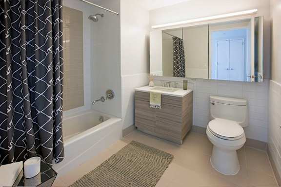 A bathroom with a white toilet, a sink, and a bathtub with a grey shower curtain at The Maximilian Apartments, New York, 11101