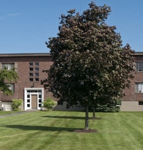 a large brick building with a lawn and trees in front of it