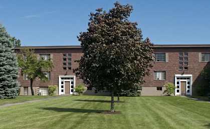 a large brick building with a lawn and trees in front of it