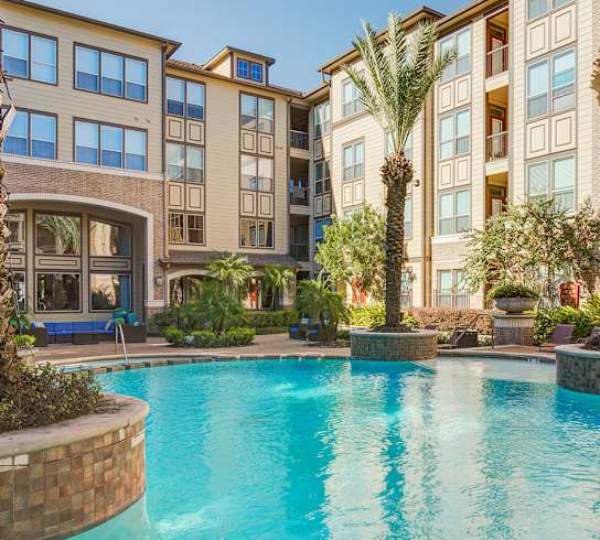 A large swimming pool in front of a multi-story apartment building.