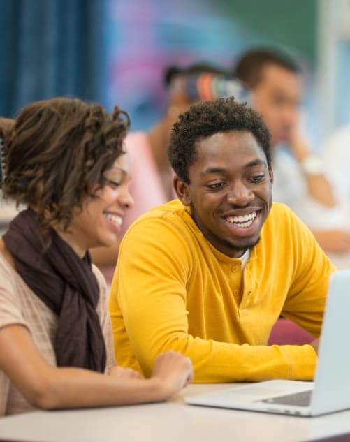 a group of students sitting at a table looking at a laptop