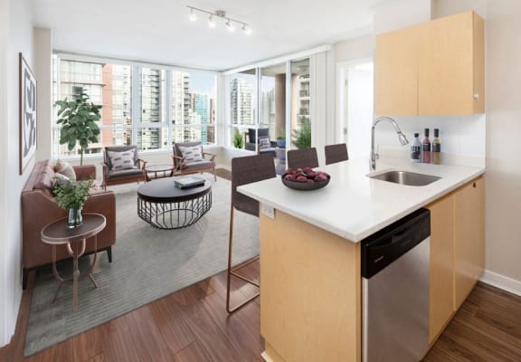 Image of a staged suite, the view is from the kitchen looking over the coffee table back to the dining room. The furniture is a contemporary adaptation of the mid-century modern style.  In this image, the TV mounted on the wall is visible.