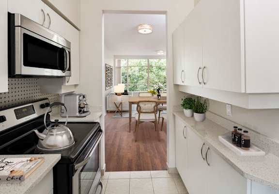 Image of a staged suite, the view is from the kitchen looking over the coffee table back to the dining room. The furniture is a contemporary adaptation of the mid-century modern style.  In this image, the TV mounted on the wall is visible.