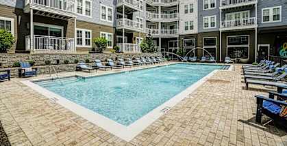 A large outdoor swimming pool surrounded by a brick patio and lounge chairs.