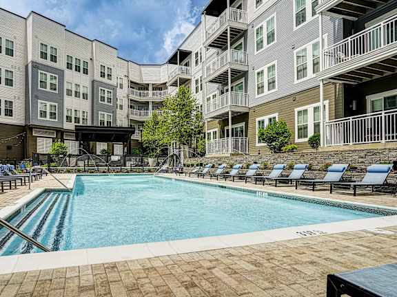 a swimming pool with lounge chairs in front of an apartment building at Lyric at Norton Commons Apartments, Prospect, Kentucky