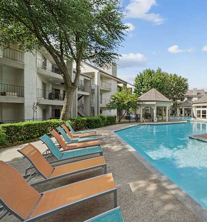A pool surrounded by lounge chairs and trees.