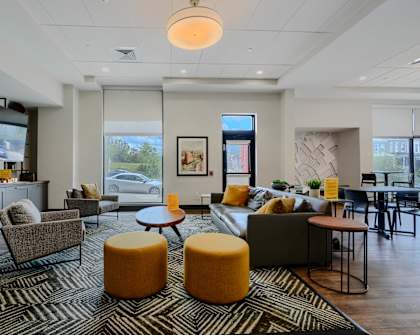 A living room with a grey couch, a yellow ottoman, and a television.