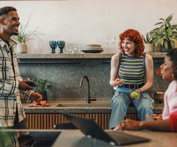 Three people are sitting and standing in a kitchen.