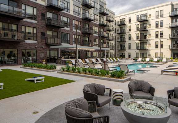 an outdoor lounge area with chairs and a fire pit in front of apartment buildings