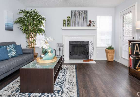 A living room with a grey couch, a glass coffee table, a fireplace, and a plant. at Wildwood Apartments , Austin, TX, 78752