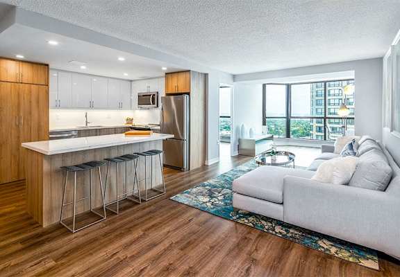 Image of a staged suite, the view is from the kitchen looking over the coffee table back to the dining room. The furniture is a contemporary adaptation of the mid-century modern style.  In this image, the TV mounted on the wall is visible.
