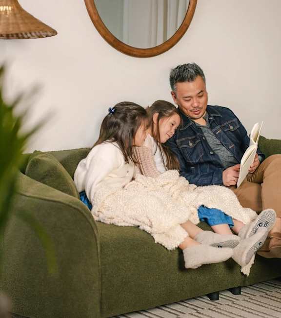 A man and two children are sitting on a green couch.