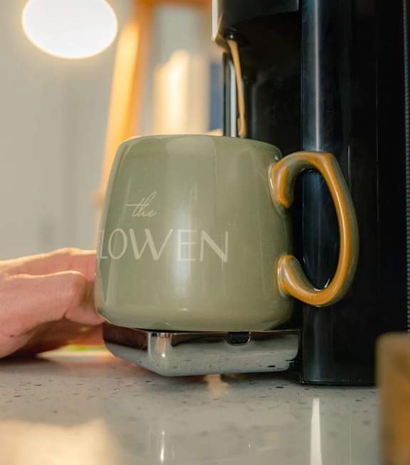 A person is holding a green mug with the word "LOWEN" on it.
